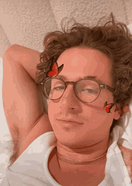 a man wearing glasses and a choker has two butterflies on his face
