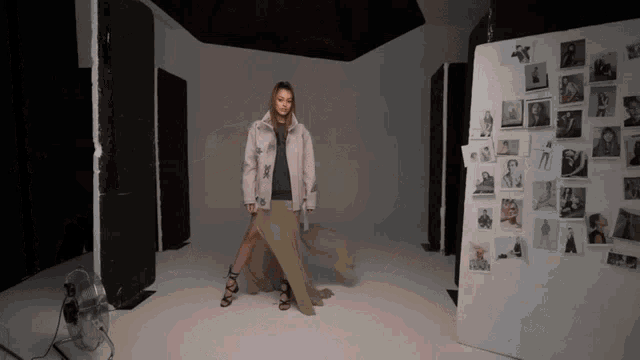 a woman in a long skirt is standing in front of a wall full of pictures