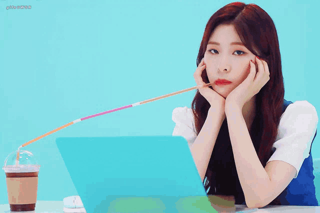 a woman is sitting in front of a laptop with a straw in her mouth