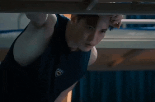 a man in a black tank top is standing under a bed .