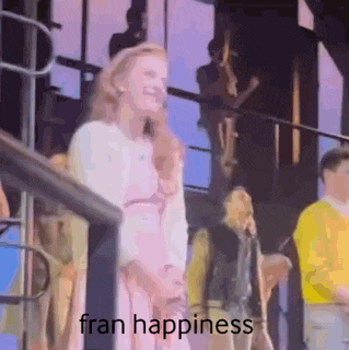 a woman in a pink dress is standing in front of a group of people and laughing .