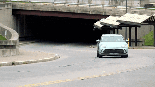 a white car is driving down a street under a bridge