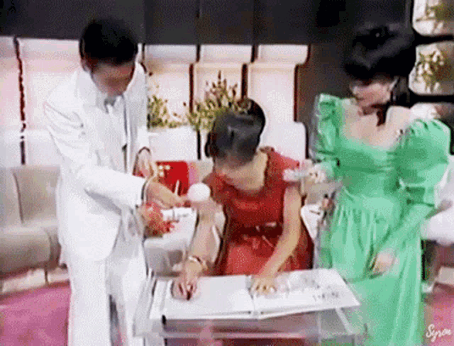 a man in a white suit and a woman in a green dress are looking at a photo album .