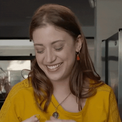 a woman wearing a yellow shirt and a necklace smiles for the camera