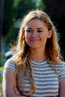 a woman wearing a striped shirt and necklace smiles with her arms crossed