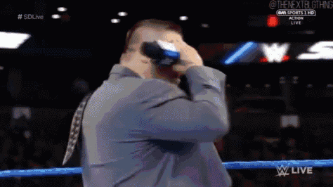 a man in a suit is standing in a wrestling ring holding a bottle of beer .