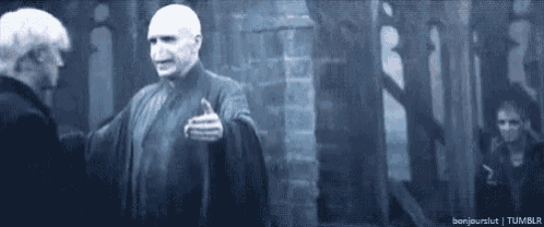 two men are standing next to each other in a dark room . one of the men is giving a thumbs up .