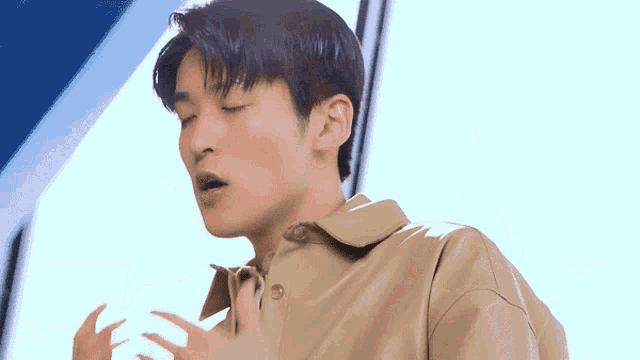 a close up of a man wearing a tan jacket with his eyes closed and his hands outstretched .