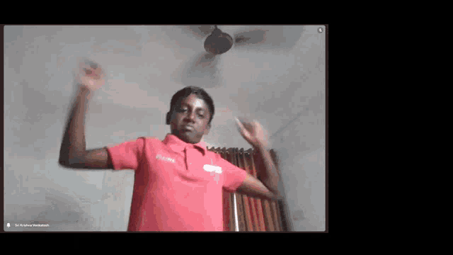 a man in a red shirt is dancing in a room with a ceiling fan behind him