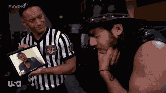 a referee holds up a picture of a wrestler while another wrestler looks down