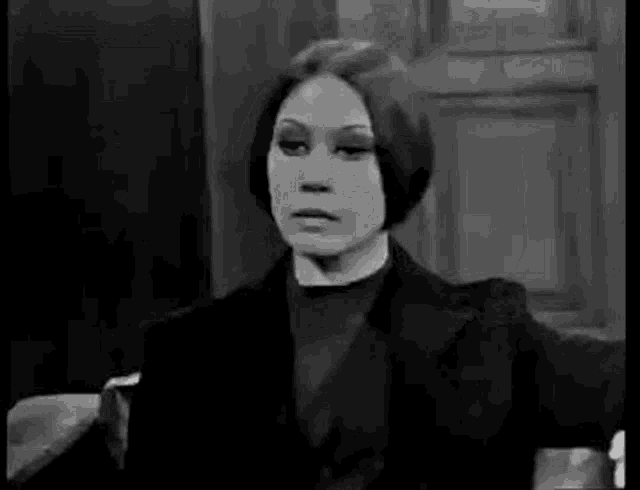a black and white photo of a woman talking on a phone in a room .