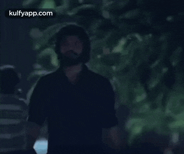 a man with a beard and a helmet on his head is walking in the dark .