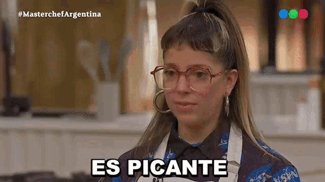 a woman wearing glasses says " es picante " while sitting in a kitchen