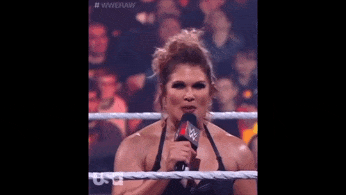a woman is standing in a wrestling ring holding a microphone and talking into it .