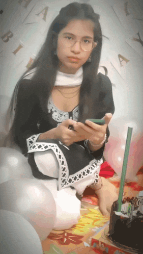 a girl is sitting in front of a birthday cake and balloons