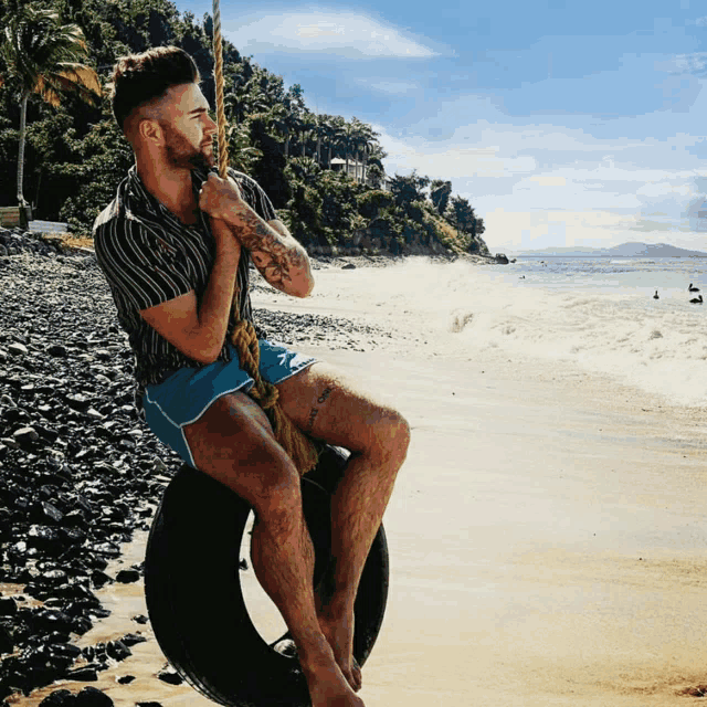 a man sitting on a tire swing on the beach