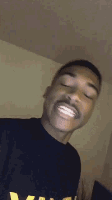 a young man in a black t-shirt is making a funny face while looking at the camera .