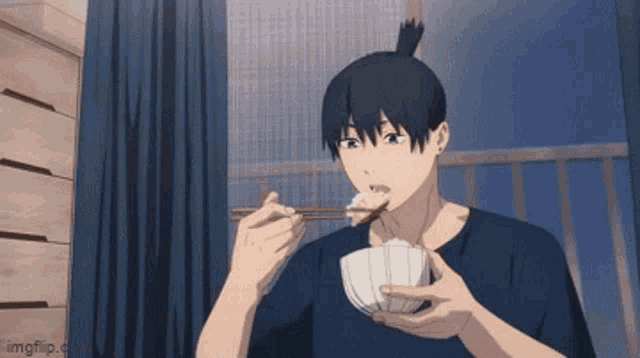 a man in a blue shirt is eating rice with chopsticks from a bowl