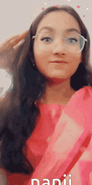 a woman wearing glasses and a pink dress is making a face .