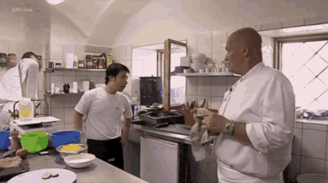 a man in a white shirt stands in a kitchen talking to another man with the word prime on the bottom right