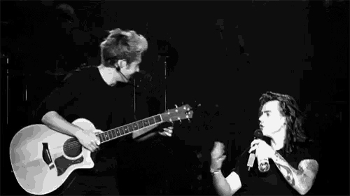 a man is playing a guitar and another man is singing into a microphone on a stage .