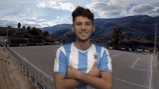 a man in a blue and white striped shirt stands with his arms crossed on a soccer field