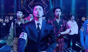 a group of men are standing on a stage in front of a crowd . one of the men is wearing a suit and tie .