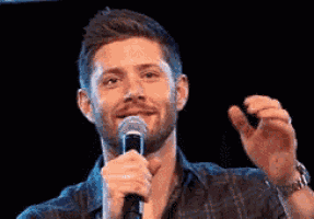 a man with a beard is holding a microphone in front of him and smiling .