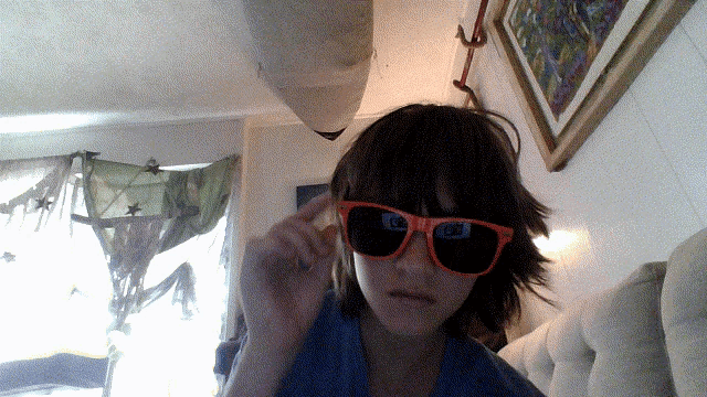a person wearing orange sunglasses in front of a painting on the wall