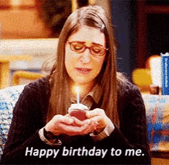 a woman is holding a cupcake with a lit candle and says happy birthday to me