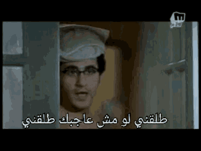 a man wearing glasses and a hat is standing in a doorway with arabic writing on it .
