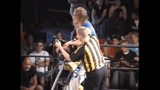 a referee is standing next to a wrestler in a wrestling ring while a crowd watches .