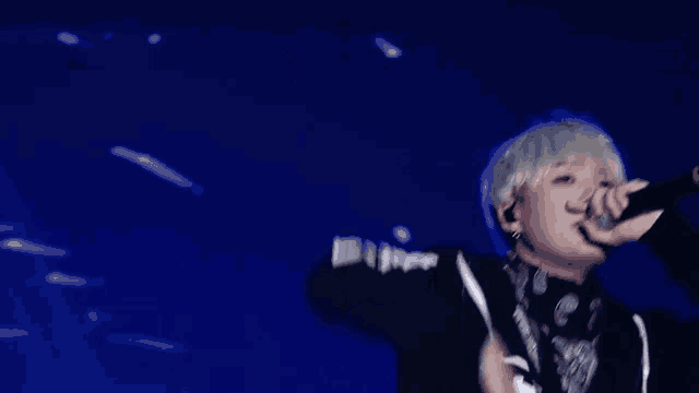 a man is singing into a microphone on a stage in front of a blue background .