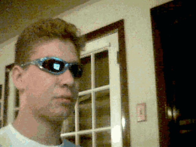a man wearing sunglasses stands in front of a white door