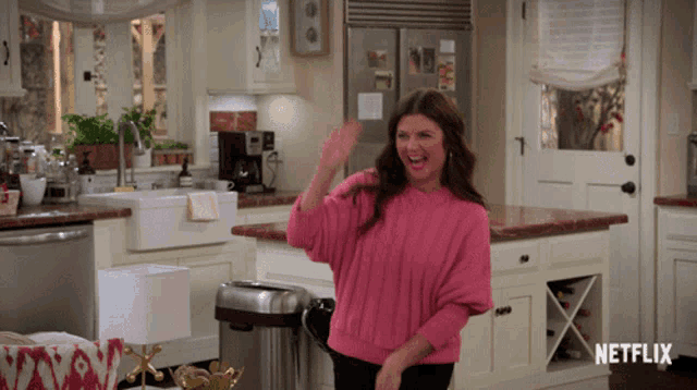 a woman in a pink sweater is dancing in a kitchen with netflix written on the bottom right
