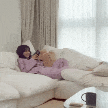 a woman is laying on a white couch holding a stuffed animal
