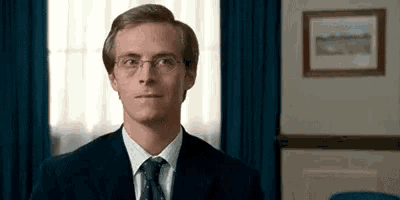 a man in a suit and tie is standing in a room with a picture on the wall .