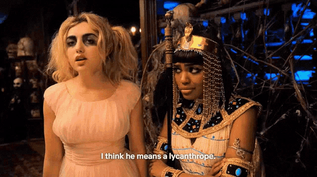 two women in costumes are standing next to each other and one of them is saying i think he means a lycanthrope
