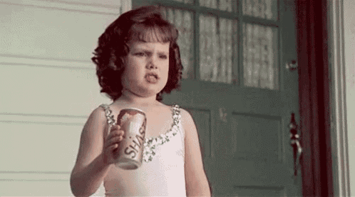a little girl in a pink dress is holding a can of soda .