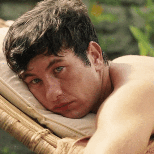 a shirtless man laying on a wicker chair with his head resting on a pillow