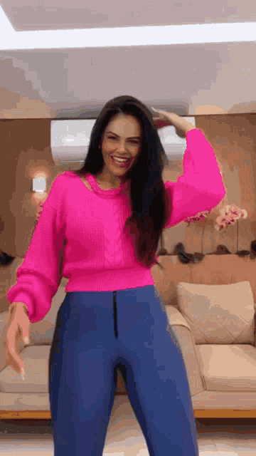 a woman wearing a pink sweater and blue pants is standing in a living room .