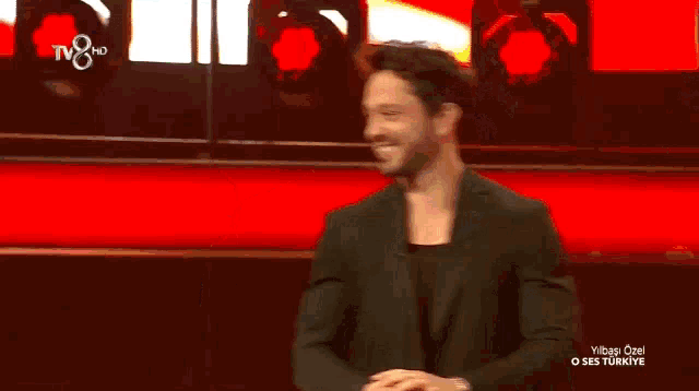 a man in a black suit is smiling in front of a red wall that says tv8 hd on it