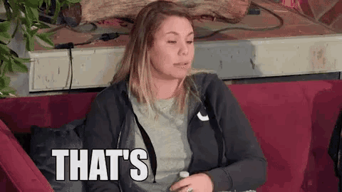 a woman is sitting on a red couch with the words `` that 's '' written on her face .