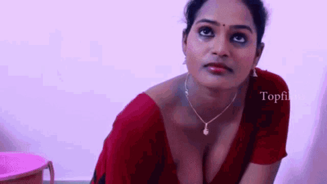 a woman in a red blouse with a plunging neckline is kneeling down and looking at the camera .