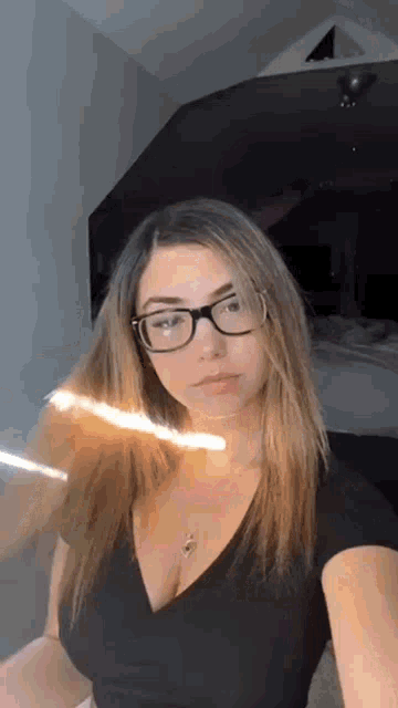 a young woman wearing glasses and a black shirt is taking a selfie .