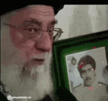 a man with glasses and a beard is looking at a picture of a man .