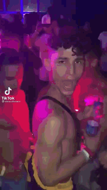 a man without a shirt is dancing in a club while another man looks on .