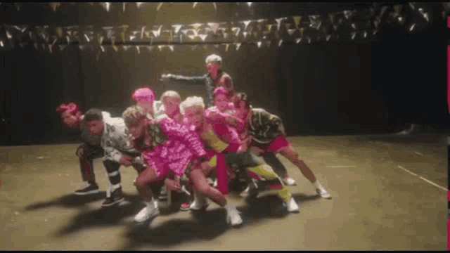 a group of people are dancing on a stage and one of them is wearing a pink dress