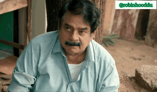 a man with a mustache is sitting under a tree with a robinhooddu logo in the upper right corner