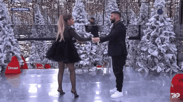 a man and a woman are dancing in front of christmas trees and a donald bag
